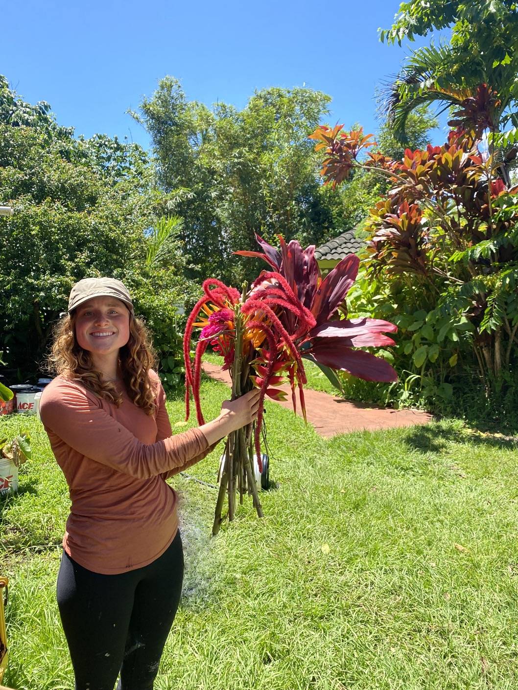 Farm intern Leanne holding a flower arrangement at the organic farm w/ lush tress in background